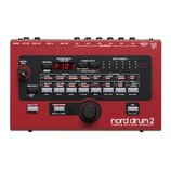 Červený perkusní syntetizátor s nápisem nord drum 2 modeling percussion synthesizer. Zařízení má digitální displej zobrazující hodnotu P1.01, několik…