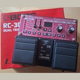 Červený pedalboard s nápisy RC-30 DUAL TRACK LOOPER a Loop Station. Zařízení má ovládací prvky pro LOOP FX, MEMORY, RHYTHM a MIC, včetně dvou černých…