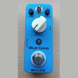 Modrý kytarový efekt s nápisem Blue Comp a značkou MOOGER. Na horní straně jsou dva černé otočné knoflíky s popisky LEVEL a ATTACK, přepínač Treble/N…