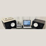 Fotografie zachicuje pracovní stůl s hudební technikou. Vlevo je bílá rytmická sekvenční jednotka s nápisem Roland TR-707, umístěná na černém studiov…