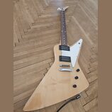 Elektrická kytara s přírodním dřevěným povrchem a bílým plechtrátem. Nástroj má dva humbuckery, jeden tónový potenciometr a jeden přepínač. Na hředel…