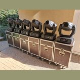 Šest kusů černých moving head světel umístěných na šesti odpovídajících transportních kufrech s kovovými hranami a kolečky. Na základnách světel jsou…