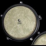 Fotografie zachycuje horní pohled na buben s béžovou membránou a černým obručem. Uprostřed membrány je logo s nápisem TOCA PERCUSSION a textem COMMUT…