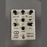 Stříbrný efektový pedál s nápisy AUDIO EVENT a DREAMY DELAY. Zařízení má šest černých otočných knoflíků s popisky delay time, delay, speed, feedback,…