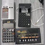 Fotografie zobrazuje tři zařízení značky Korg a doprovodné příslušenství. V horní části je stříbrný kartonový obal s nápisy pocket operator PO-33 K O…