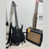 Černá elektrická kytara s matným povrchem a černým popruhkem, umístěná na stojanu. Na hlavě kytary je viditelné logo "Ibanez". Vedle kytary stojí mal…