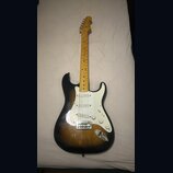 Elektrická kytara s tónem těla v provedení sunburst a bílým pickguardem. Na hlavě hředu je viditelné logo Fender. Nástroj má javorový hmatník a tři s…