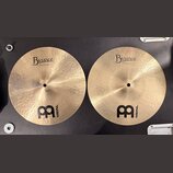 Dvě mosazné činely s viditelným broušením a hloubkovým rýhováním. Oba mají nápisy Byzance a logo MEINL. Na levém číneli je text 13" Medium Hihat, Bot…