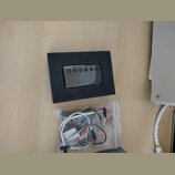 Černý obdélníkový modul s nápisem EMG a pěti kulatými ovládacími prvky. Pod modulem je průhledný plastový sáček s elektroinstalací, kabely a drobnými…