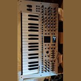 Bílý syntetizátor s klaviatura značky Roland, model GAIA 2. Přístroj má numerous ovládací prvky v podobě posuvníků, otočných knoflíků a tlačítek, vče…