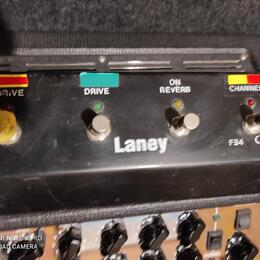 Černý spínací pedál značky Laney s třemi kovovými spínači. Nad spínači jsou nápisy DRIVE, ON REVERB a CHANNEL, přičemž u prvního a posledního jsou če…