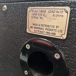 Detail zadní strany kytarového reproboxu s černým texturovaným povrchem. Na kovovém štítku je uveden nápis: Model 1965B LEAD 4x10", 140W R.M.S., 8 oh…