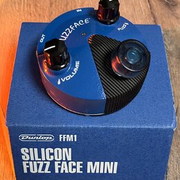 Modrý kytarový efekt v kruhovém šasi s černým žebrovaným ovládacím prvkem a dvěma černými knoflíky. Na horní straně jsou nápisy FUZZFACE, VOLUME a oz…