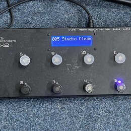 Černý MIDI kontrolér s nápisy VOES Midi Controllers a MX-12. Zařízení má modrý displej s textem 005 Studio Clean a dvanáct tlačítek označených čísly…
