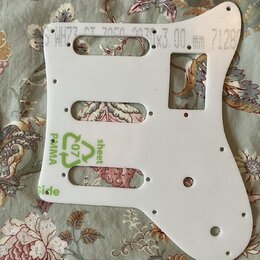 Bílá plastová pickguard pro kytaru s několika otvory a výřezy. Na povrchu jsou viditelné zelené nápisy „sheet“, „Side“ a symbol recyklace s číslem „0…