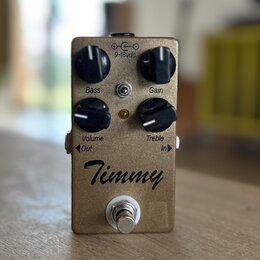 Kytarový efekt pedál v bronzové barvě s kovovým povrchem. Na přední straně jsou čtyři černé otočné knoflíky s popisky Bass, Gain, Volume a Treble. Up…