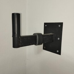 Černý nástěnný držák na hudební nástroj vyrobený z kovových trubek a ploché základny. Horní část je potažena černým materiálem, podobně jako opora v…