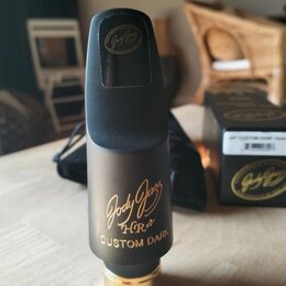 Černý saxofonový mouthpiece s matným povrchem a zlatým kovem v dolní části. Na přední straně je zlatý nápis „Jody Jazz HR* CUSTOM DARK“. V horní část…