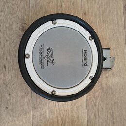 Kruhové elektronické bubnové plochy s bílým pleteným povrchem a černým gumovým okrajem. Na povrchu jsou nápisy Roland, MESH HEAD™ made by REMO a logo…