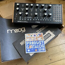 Semi-modulární analogový syntetizátor v dřevěném šasi s černým ovládacím panelem. Na přední straně je nápis MOTHER-32 SEMI-MODULAR ANALOG SYNTHESIZER…