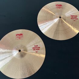 Dvě stříbrné činely z mosazi s viditelným broušením povrchu. Na levém číneli je červený nápis PAISTE 2002 MADE IN SWITZERLAND a text TOP MEDIUM HI-HA…