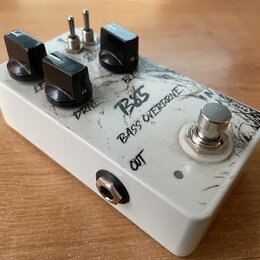 Bílý efekt pedál s nápisy BASS a BASS OVERDRIVE. Na horní straně jsou tři černé oválné knoflíky s popisy LEVEL, DRIVE a BLEND, dva malé přepínače a j…
