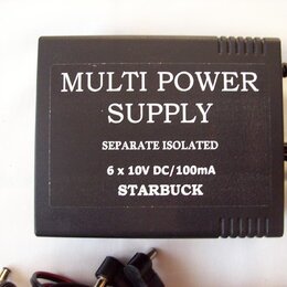 Černý hranatý zdroj napájení s textem MULTI POWER SUPPLY, SEPARATE ISOLATED a 6 x 10V DC/100mA. Dole je uveden nápis STARBUCK. Povrch zařízení má jem…