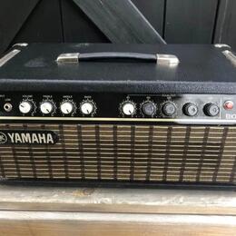 Černý kytarový kombo zesilovač s kovovými hranami a úchytem. Na předním panelu je nápis YAMAHA vlevo u mřížky a modelové označení B100II vpravo. Ovlá…