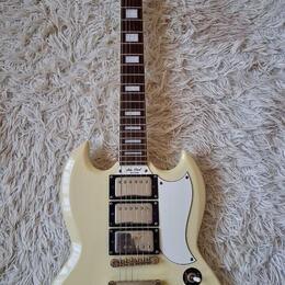 Krémově bílá elektrická kytara typu SG značky Epiphone. Na hlavě je nápis Epiphone a na krytce snímačů text Les Paul Special. Nástroj má dva humbucke…