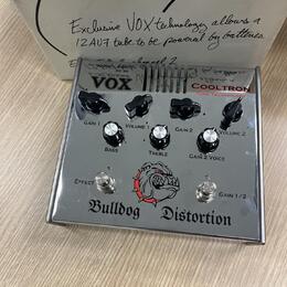 Stříbrný efekt pedál s nápisem Bulldog Distortion a logem hlavy buldoka. Na horním panelu je značka VOX a nápis COOLTRON TUBE TECHNOLOGY. Zařízení má…
