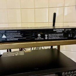 Zadní strana černého rackového zařízení s nápisem ALLEN&HEATH AR0904 AudioRack. Na šasi jsou umístěny various varovné štítky s nápisy CAUTION, RISK O…