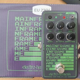 Šedý efekt pedál s nápisy MAINFRAME, bit crusher a značkou electro-harmonix NEW YORK CITY, USA. Zařízení má pět černých otočných ovladačů s popisky V…