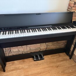 Černý digitální piano s bílými a černými klávesami, umístěné na černém dřevěném stojanu. Nástroj má otevřenou horní krytovku a v dolní části je umíst…
