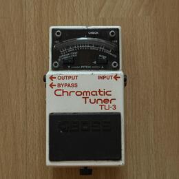 Bílý ladicí pedál s nápisy OUTPUT, BYPASS a Chromatic Tuner TU-3. V horní části je displej s označením CHECK, stupnicí od -50 do +50 a nápisy STREAM/…