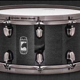 Černý snare drum s kovovými obručemi a mechanismem na napnutí. Na korpusu je umístěno logo se štítem, nápisy BLACK a PANTHER a vyobrazením pantera. N…