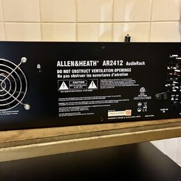 Zadní strana černého rackového zařízení s nápisem ALLEN&HEATH AR2412 AudioRack. Na šasi jsou umístěny varovné štítky s texty CAUTION, RISK OF ELECTRI…