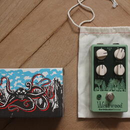 Zelený efekt pedál s nápisy Level, Drive, Bass a Treble u ovládacích knoflíků. Ve spodní části je logo Westwood a text EarthQuakerDevices. Vedle pedá…