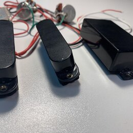 Tři černé elektrické snímače kytary s plastovými kryty. V pozadí jsou vidět zapojené potenciometry a elektrické součástky s červenými, bílými a zelen…