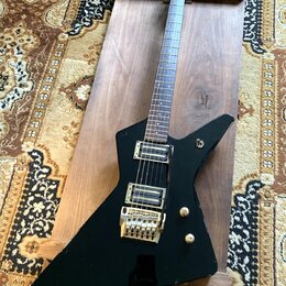 Černá elektrická kytara s ostře hranatým korpusem a hnědým hmatníkem. Na hlavě je nápis "Ibanez". Nástroj má dva humbuckery se zlatými kryty a zlatý…