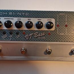 Stříbrný basový předzesilovač s nápisem TECH 21 NYC a označením VT Bass DELUXE. Zařízení má šest černých otočných ovladačů s popisky DRIVE, CHARACTER…