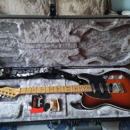 Elektrická kytara s trupem v barevnosti sunburst, černým pickguardem a světle hnědým hnedým hmatníkem. Na hlavě kytary je nápis Fender. Nástroj leží…