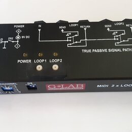 Černý kovový box s bílými nápisy a schéma zapojení na horní straně. Na přední části je logo G-LAB GUITAR LABORATORY a nápis MIDI 2 x LOOP. Zařízení m…