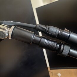 Detailní pohled na dva černé audio kabely s konektory. Jeden z nich má stříbrný kovový konektor a druhý je celý v černé barvě. Povrchy kabelů a konek…