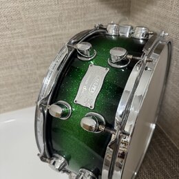 Zelený buben s glitrovým povrchem a chromovaným kováním. Na korpusu je kovový štítek s nápisy „Sultana“, „MAPEX“ a „Custom Series“. Na horním obruči…