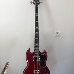 Čtyřstrunná basová kytara s červeným lesklým povrchem těla a černou hlavou. Na hlavě je nápis Epiphone. Tělo má charakteristický SG tvar, černý pickg…