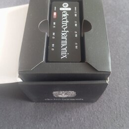 Černý napájecí adaptér značky electro-harmonix umístěný v originální černé krabici. Na zařízení je bílý nápis electro-harmonix a označení 9V u jednot…