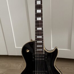 Černá elektrická kytara typu Les Paul se zlatými hardwaremi a bílými blokovými vložkami na hmatníku. Na hlavě je nápis Orville a pod ním menší text b…