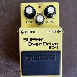Žlutý kytarový efekt pedál značky BOSS, model SUPER Over Drive SD-1. Na horní části jsou tři černé ovládací knoflíky s bílými vršky a nápisy LEVEL, T…