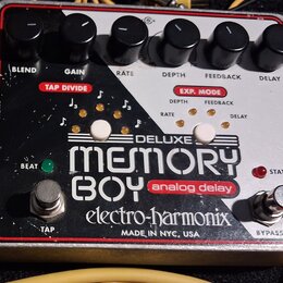 Efekt pedál analogového delay s bílo-černým povrchem a červeným rámem. Na zařízení jsou nápisy DELUXE MEMORY BOY analog delay, electro-harmonix a MAD…