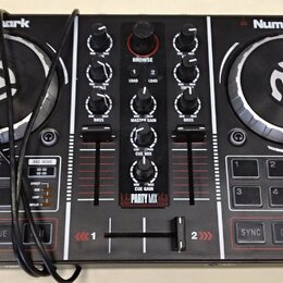 Černý DJ kontrolér značky Numark s modelem PARTY MIX. Zařízení má dva stříbrno-černé jog-wheels, středovou sekci s knoflíky a posuvníky a spodní část…